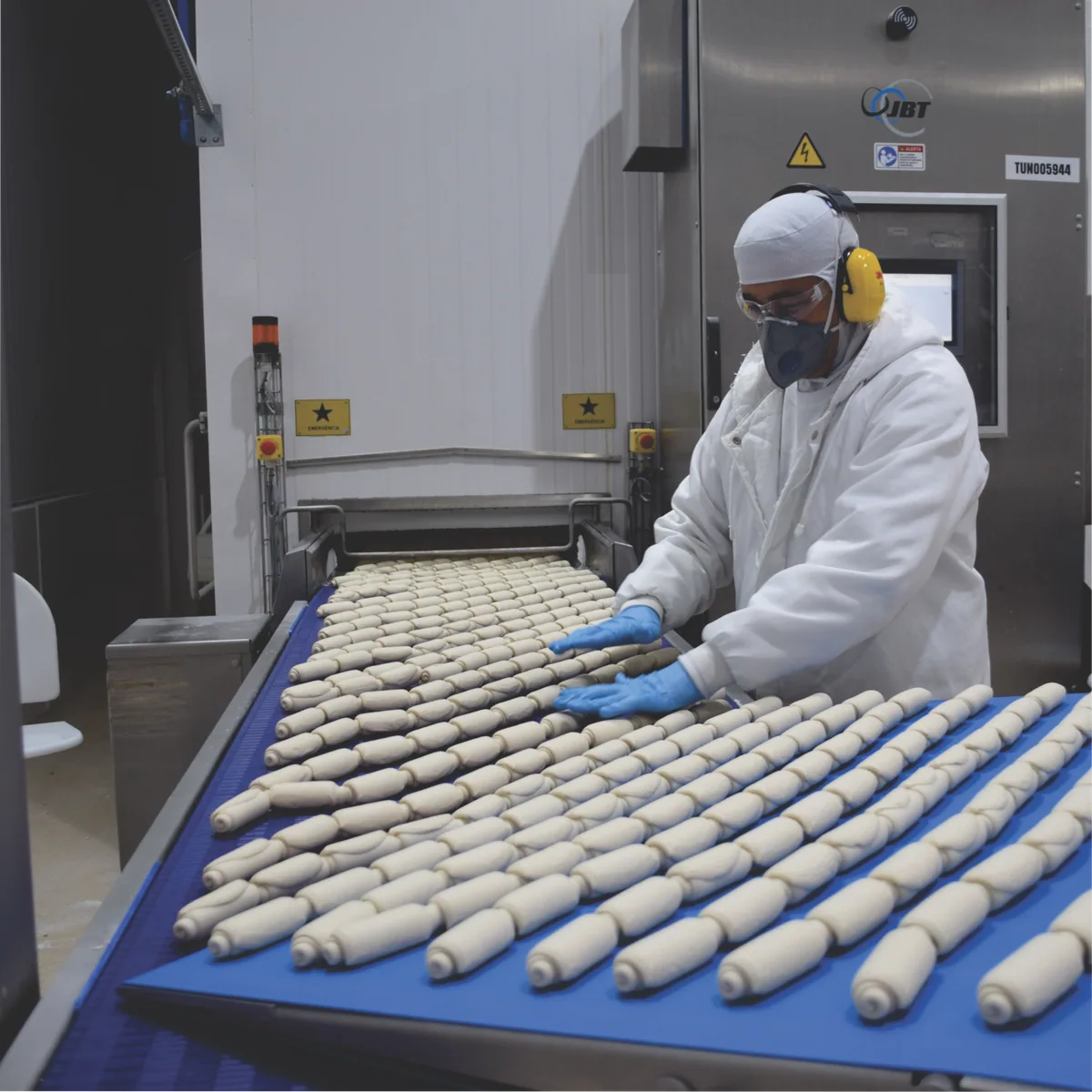 Profissional acompanhando os pães na linha de produção do Grupo Doce D’ocê